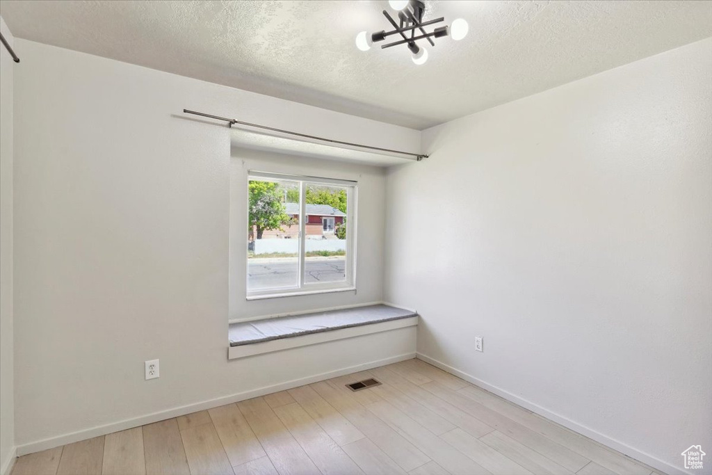 Empty room featuring visible vents, a textured ceiling, baseboards, and a chandelier