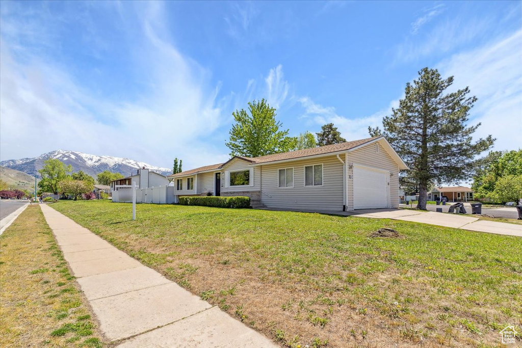 Single story home featuring a garage, fence, a front yard, a mountain view, and driveway