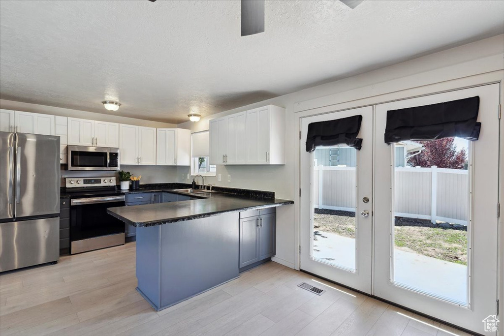 Kitchen featuring visible vents, a peninsula, dark countertops, a sink, and appliances with stainless steel finishes