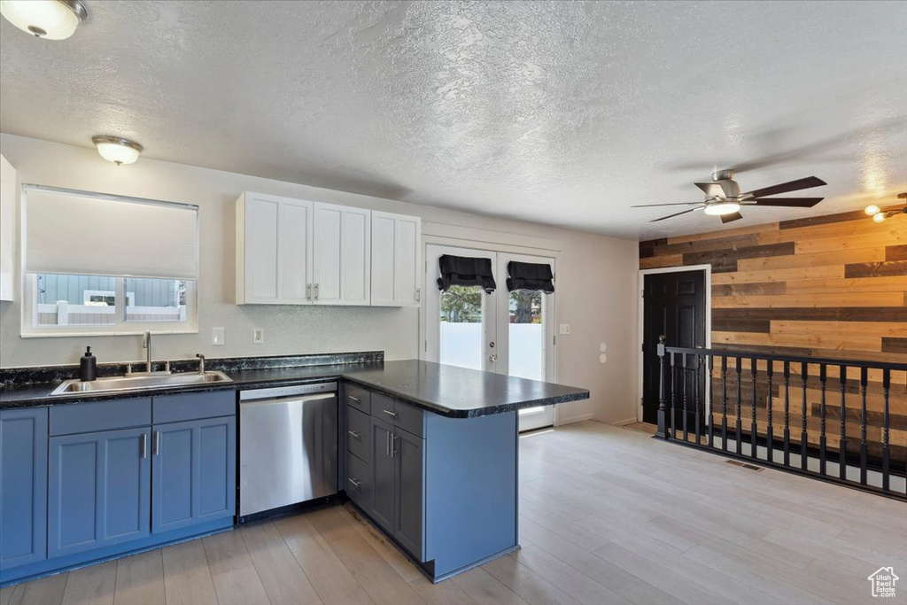 Kitchen with wooden walls, dark countertops, a sink, a peninsula, and stainless steel dishwasher