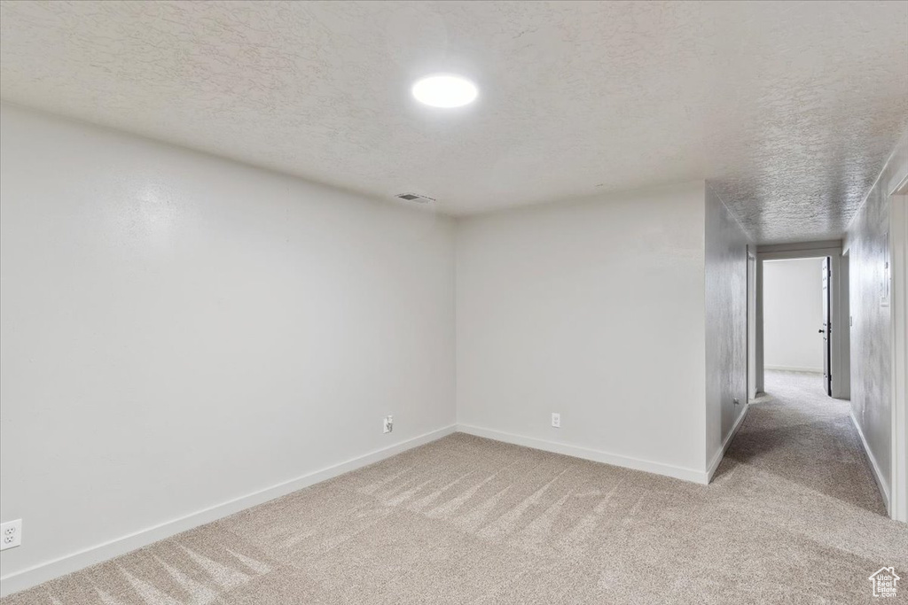 Empty room with carpet flooring, a textured ceiling, visible vents, and baseboards