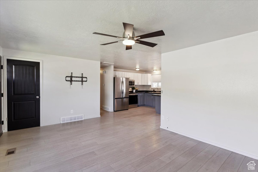 Unfurnished living room featuring a ceiling fan, light wood finished floors, a textured ceiling, and visible vents