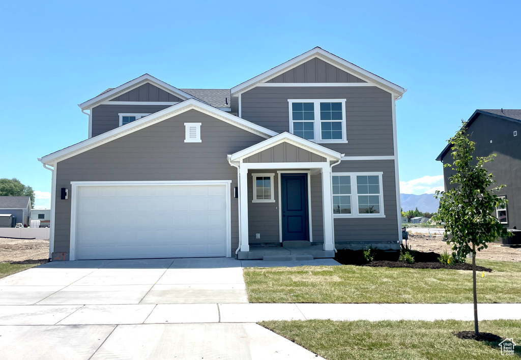 Traditional-style home with board and batten siding, an attached garage, concrete driveway, and a front yard