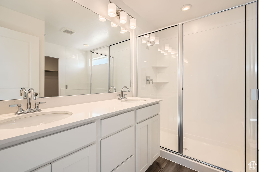 Full bath featuring a shower stall, double vanity, a walk in closet, wood finished floors, and recessed lighting