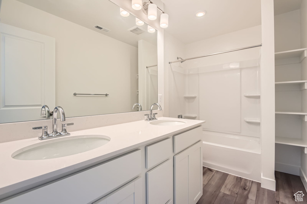 Bathroom with shower / washtub combination, double vanity, recessed lighting, and wood finished floors