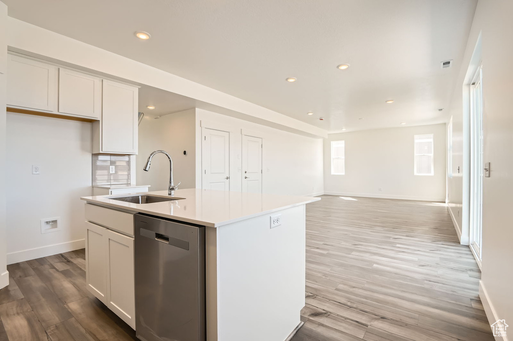 Kitchen with dishwasher, a sink, a center island with sink, baseboards, and white cabinets