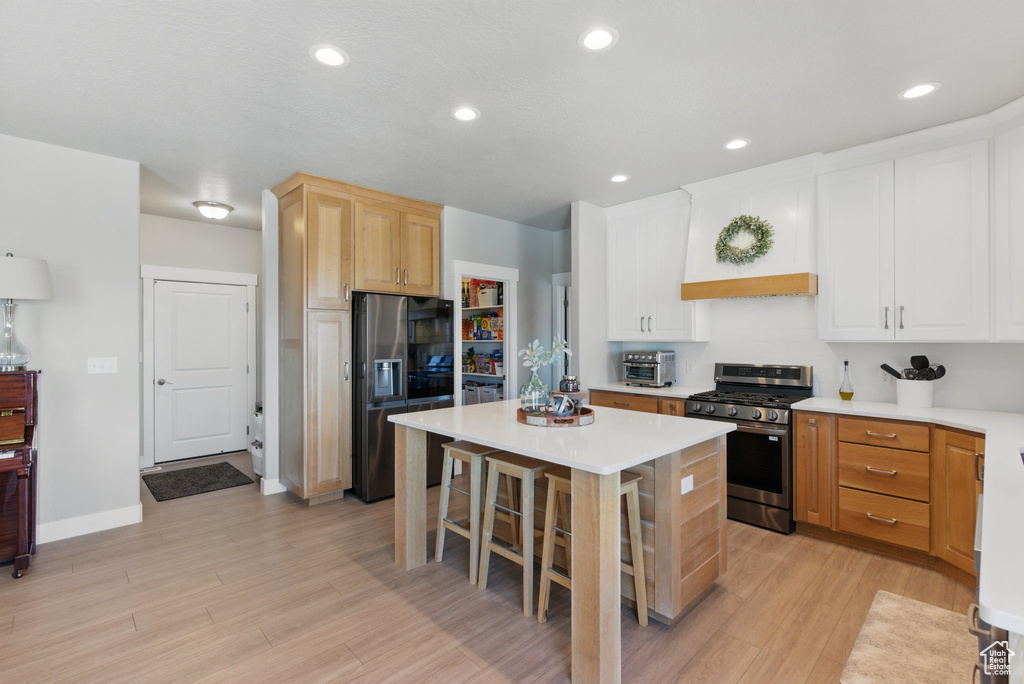 Kitchen with a kitchen island, light countertops, light wood-style floors, a breakfast bar, and stainless steel appliances