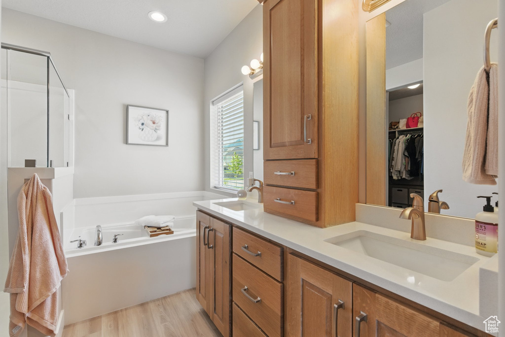Bathroom with a sink, a bath, double vanity, and wood finished floors