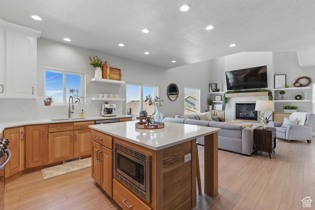 Kitchen with a glass covered fireplace, light wood-type flooring, light countertops, stainless steel microwave, and a sink