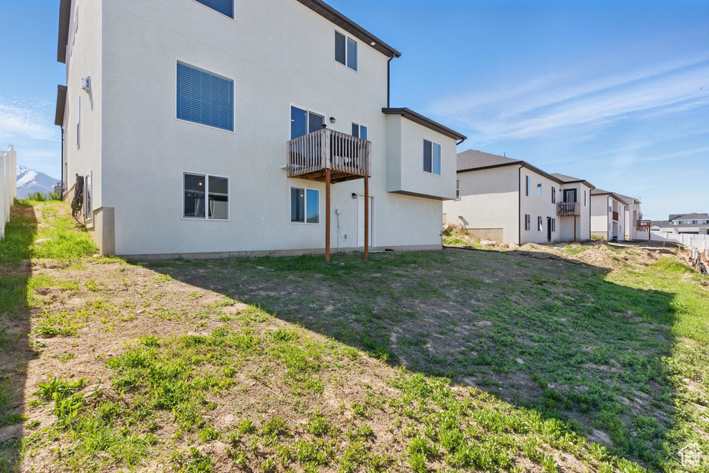 Rear view of property featuring stucco siding, a yard, and a balcony