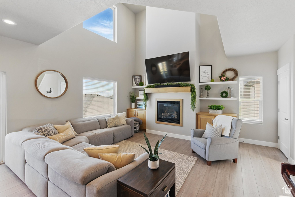 Living room featuring a glass covered fireplace, recessed lighting, baseboards, light wood-type flooring, and a towering ceiling