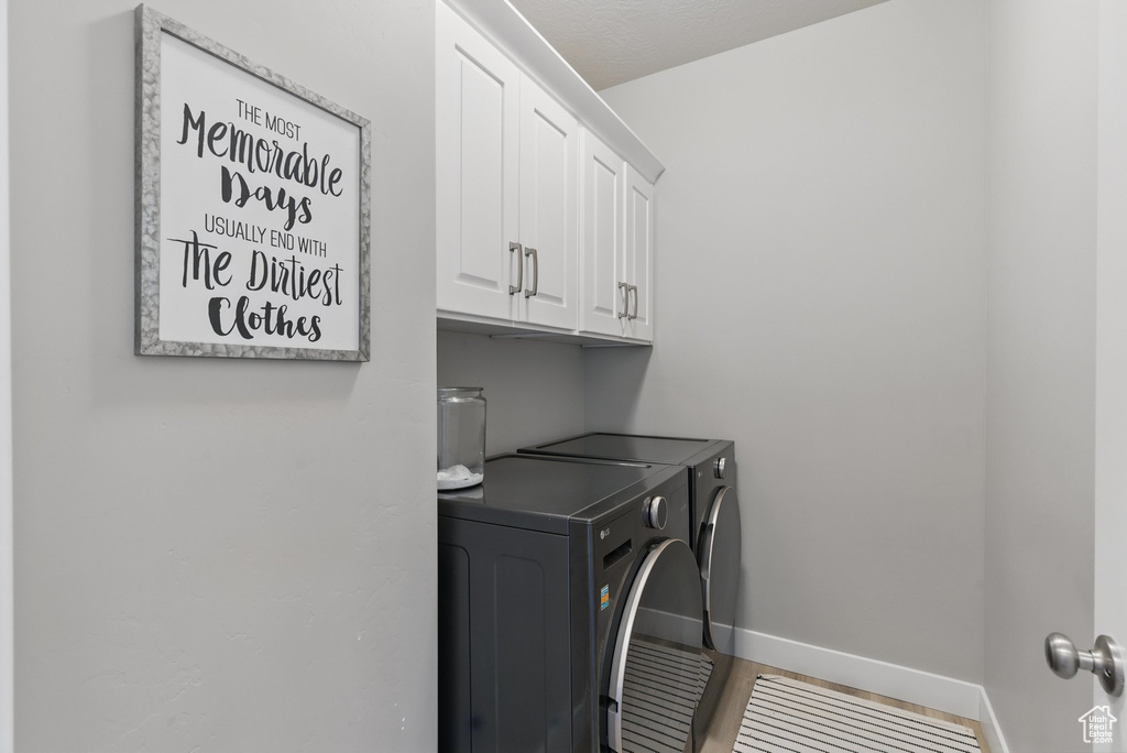 Clothes washing area with separate washer and dryer, tile patterned flooring, cabinet space, and baseboards
