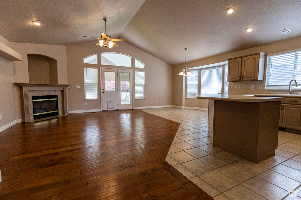 Kitchen featuring light countertops, a tiled fireplace, ceiling fan with notable chandelier, open floor plan, and vaulted ceiling