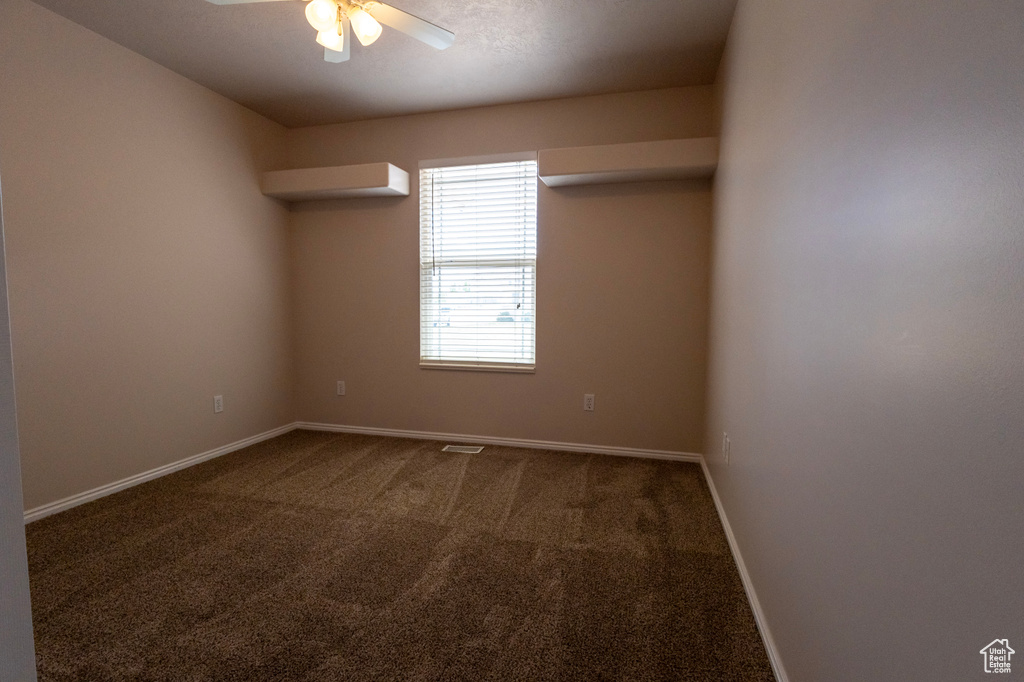 Spare room with a ceiling fan, baseboards, and dark carpet