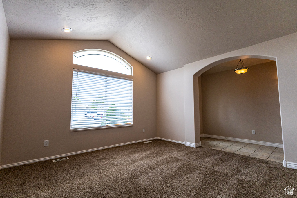 Unfurnished room with light colored carpet, arched walkways, a textured ceiling, light tile patterned floors, and vaulted ceiling