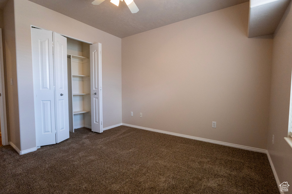 Unfurnished bedroom featuring baseboards, ceiling fan, a closet, and dark colored carpet