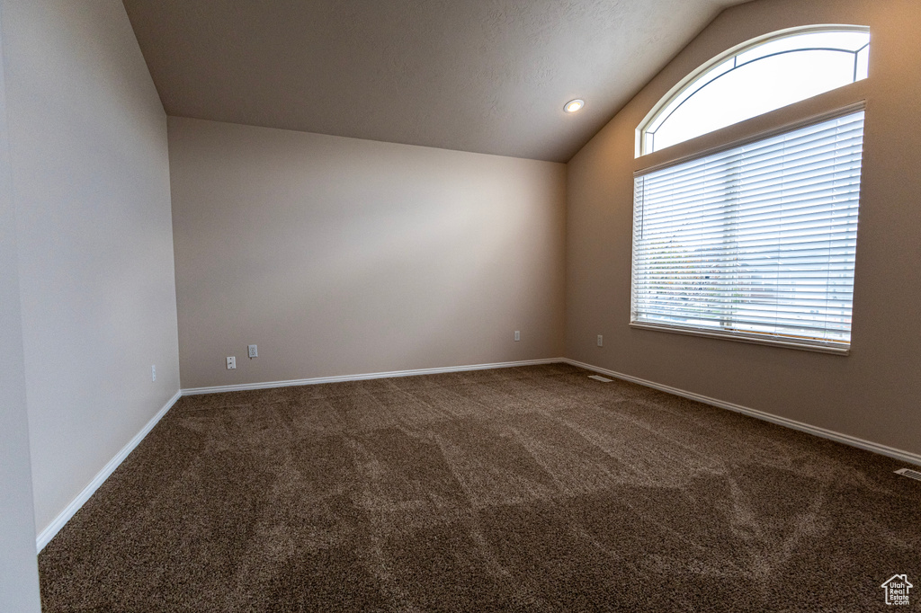 Carpeted empty room featuring baseboards, vaulted ceiling, and visible vents