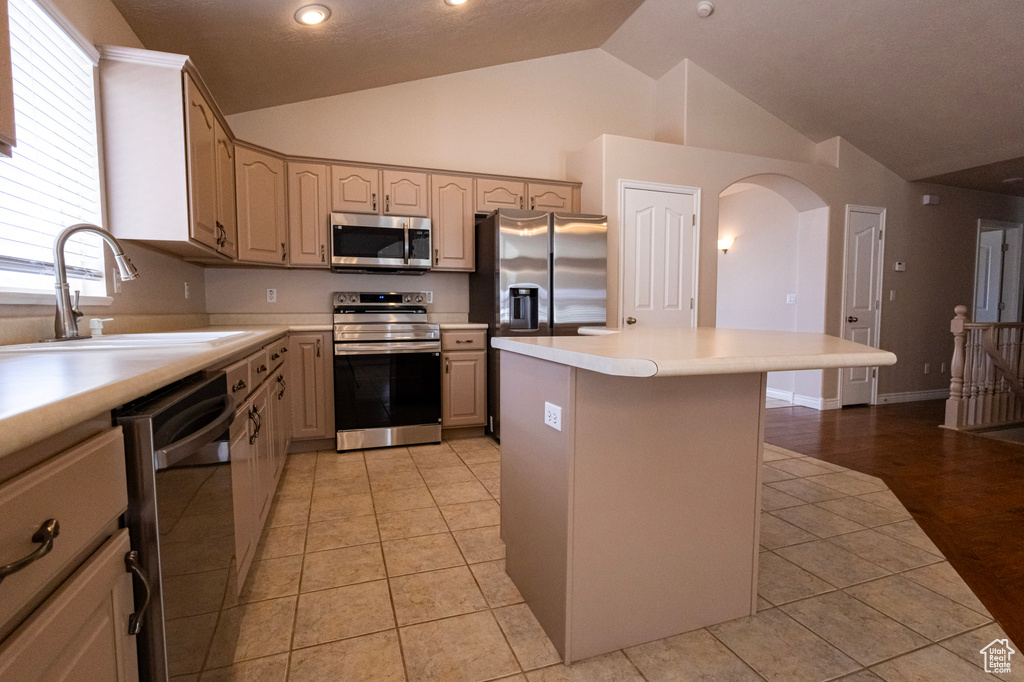 Kitchen featuring a kitchen island, arched walkways, a sink, light tile patterned floors, and stainless steel appliances