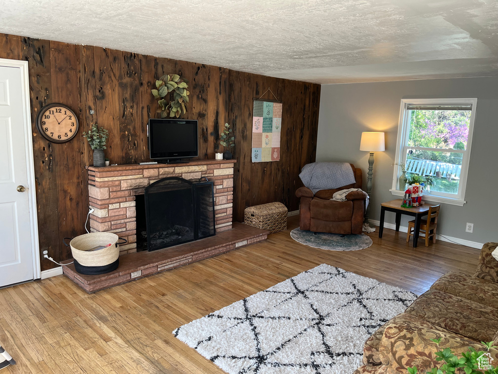 Living room with wooden walls, a fireplace with raised hearth, a textured ceiling, baseboards, and wood finished floors
