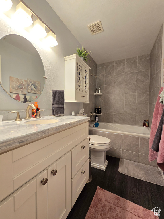 Bathroom featuring visible vents, wood finished floors, vanity, toilet, and tiled shower / bath combo