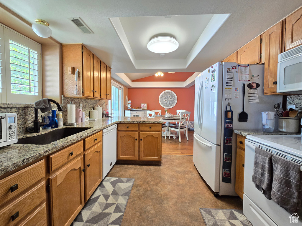 Kitchen featuring visible vents, a sink, a peninsula, a tray ceiling, and white appliances