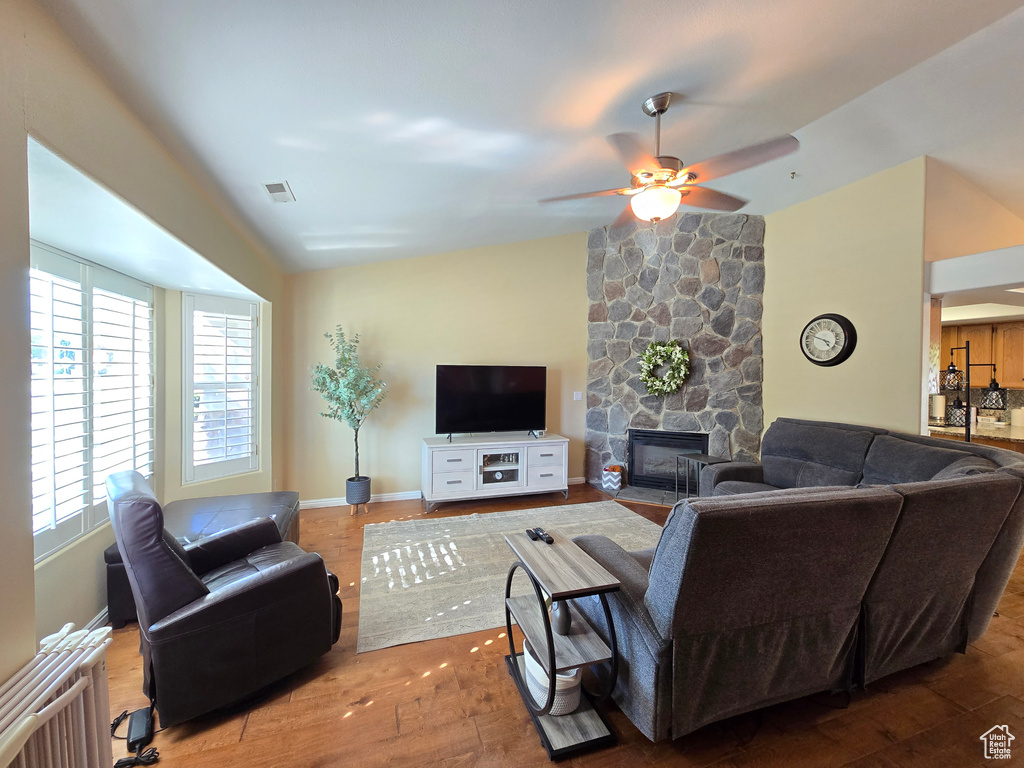 Living room with ceiling fan, a fireplace, wood finished floors, vaulted ceiling, and visible vents