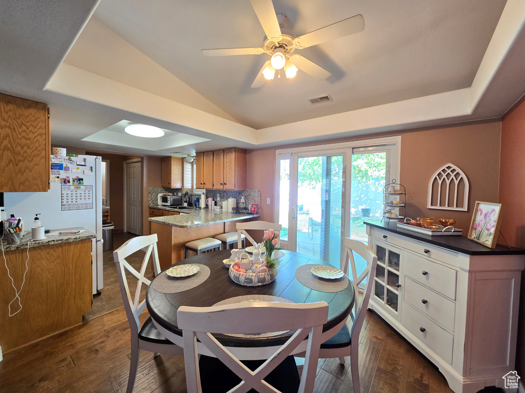 Dining area featuring visible vents, lofted ceiling, ceiling fan, dark wood-style floors, and a raised ceiling