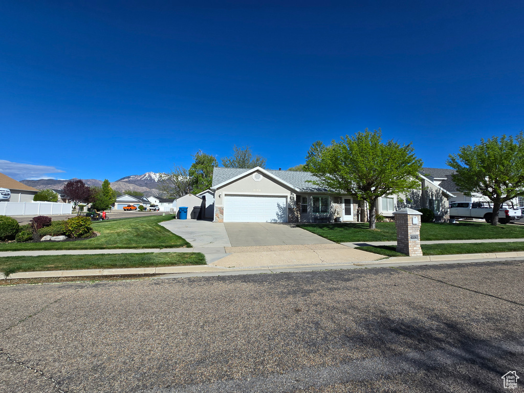 Ranch-style house with an attached garage, driveway, a mountain view, and a front lawn
