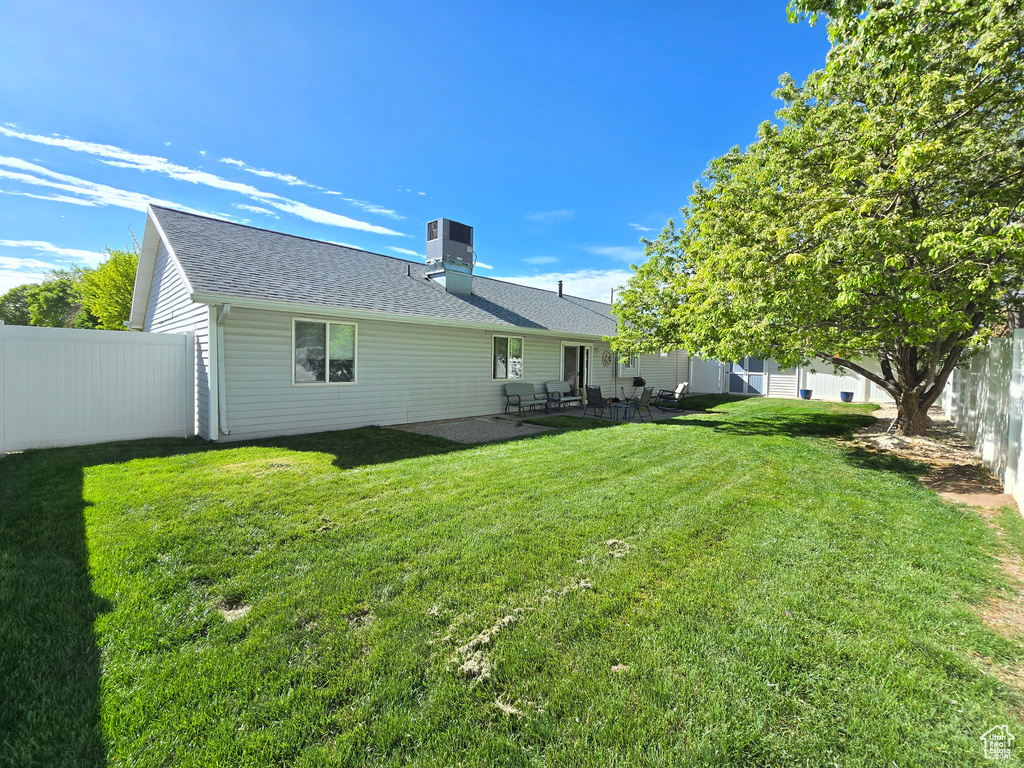 Back of house with a lawn, fence, a chimney, and roof with shingles