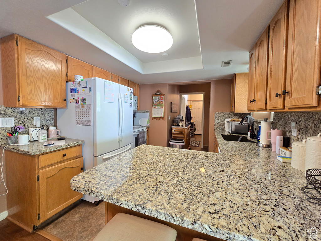 Kitchen with a raised ceiling, freestanding refrigerator, backsplash, and a peninsula