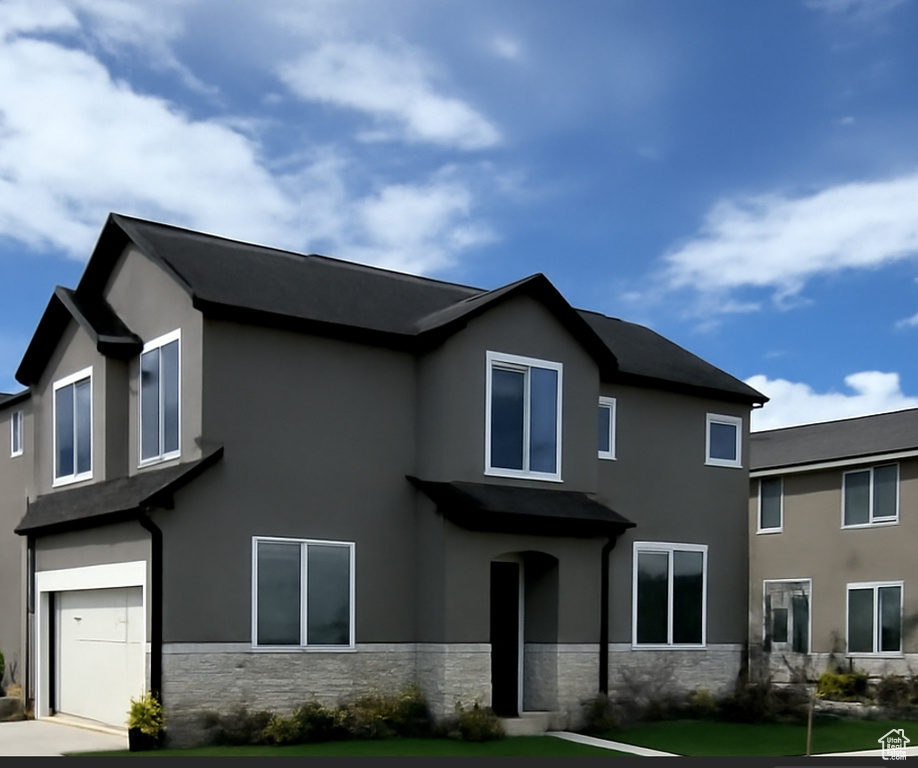 View of front of property featuring an attached garage, a front lawn, stucco siding, and stone siding