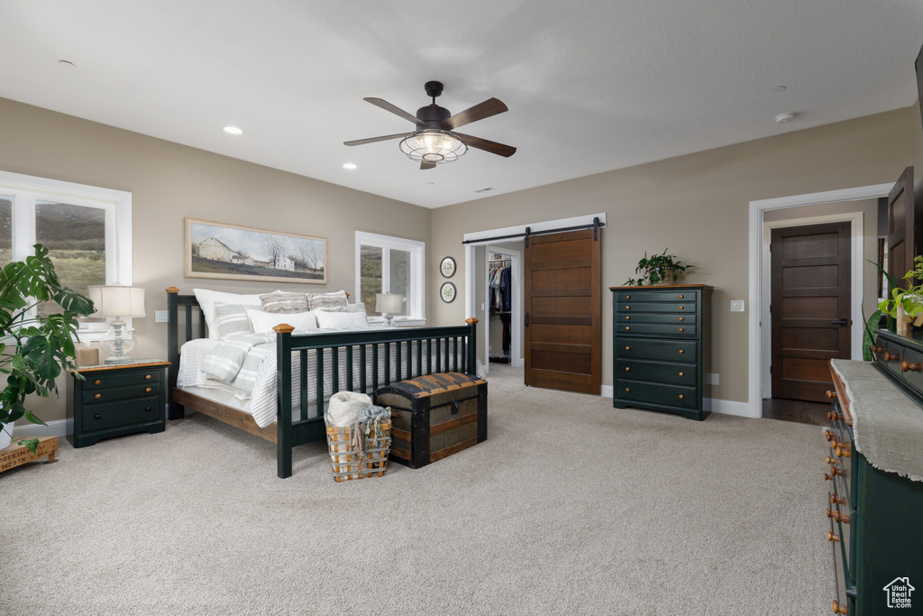 Carpeted bedroom with ceiling fan, a barn door, and a walk in closet