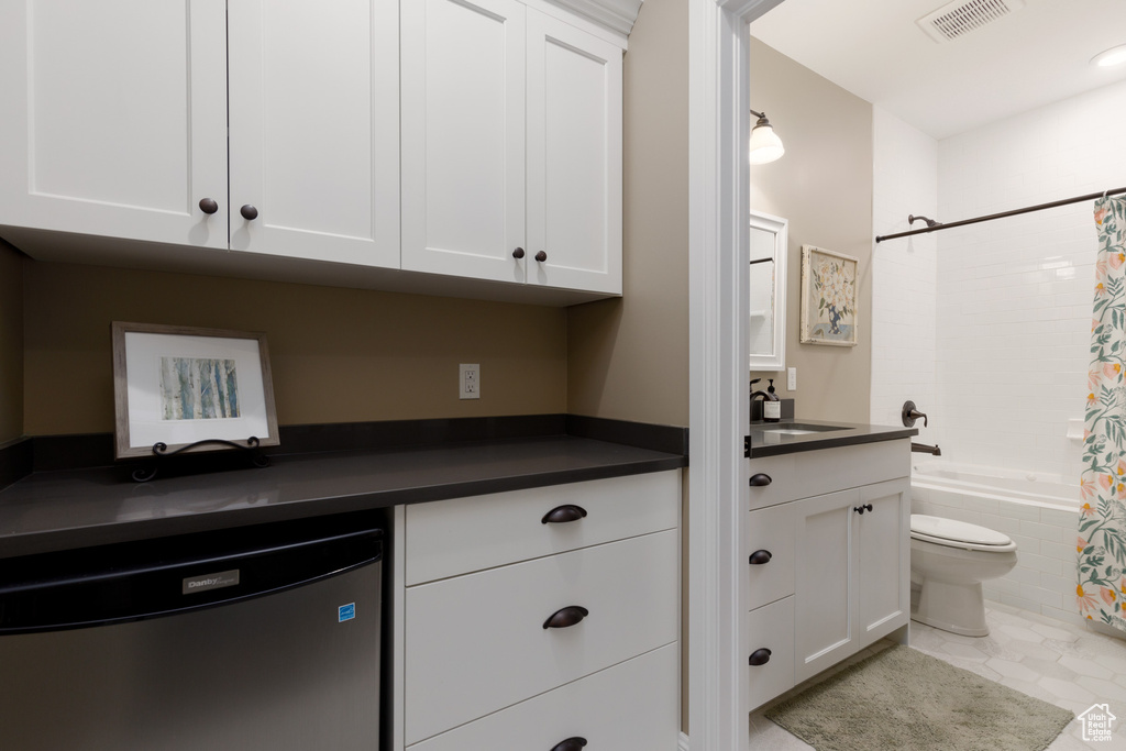 Kitchen with white cabinetry, stainless steel dishwasher, sink, and light tile patterned floors