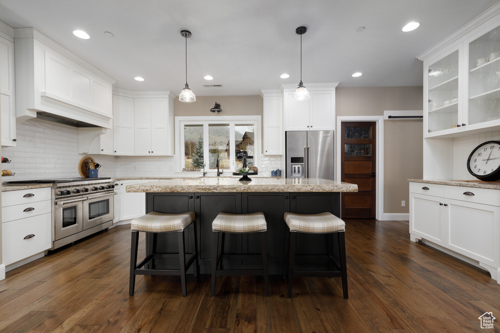 Kitchen featuring decorative light fixtures, high quality appliances, white cabinets, a kitchen bar, and a center island