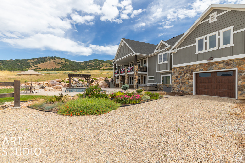 View of front of property with a garage, a balcony, a hot tub, a pergola, and a mountain view