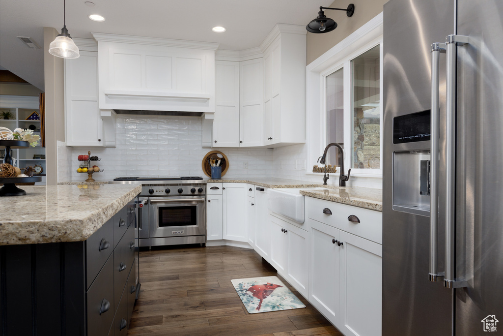 Kitchen featuring high quality appliances, sink, white cabinets, hanging light fixtures, and light stone countertops