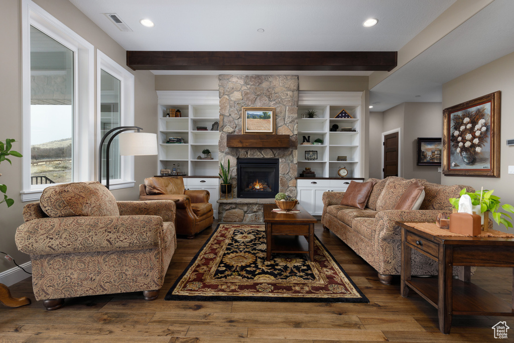 Living room featuring beam ceiling, a stone fireplace, and dark hardwood / wood-style flooring