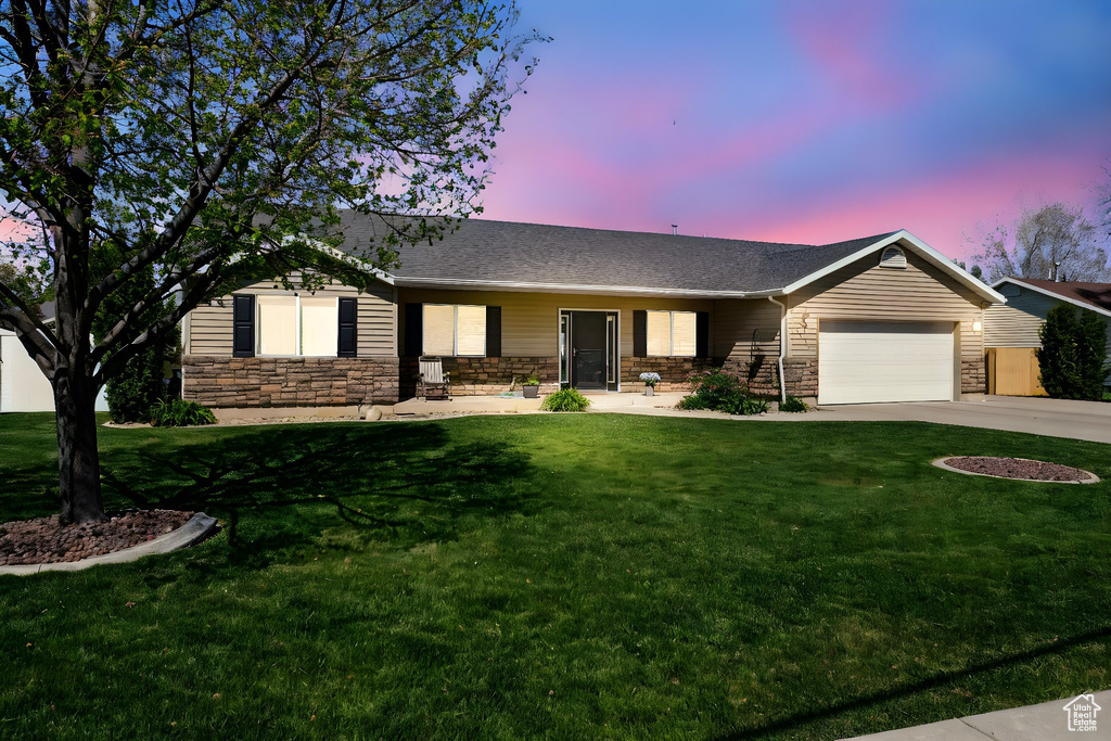 Single story home featuring an attached garage, a yard, driveway, and stone siding