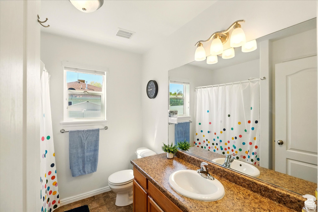 Full bathroom featuring baseboards, vanity, toilet, and a wealth of natural light