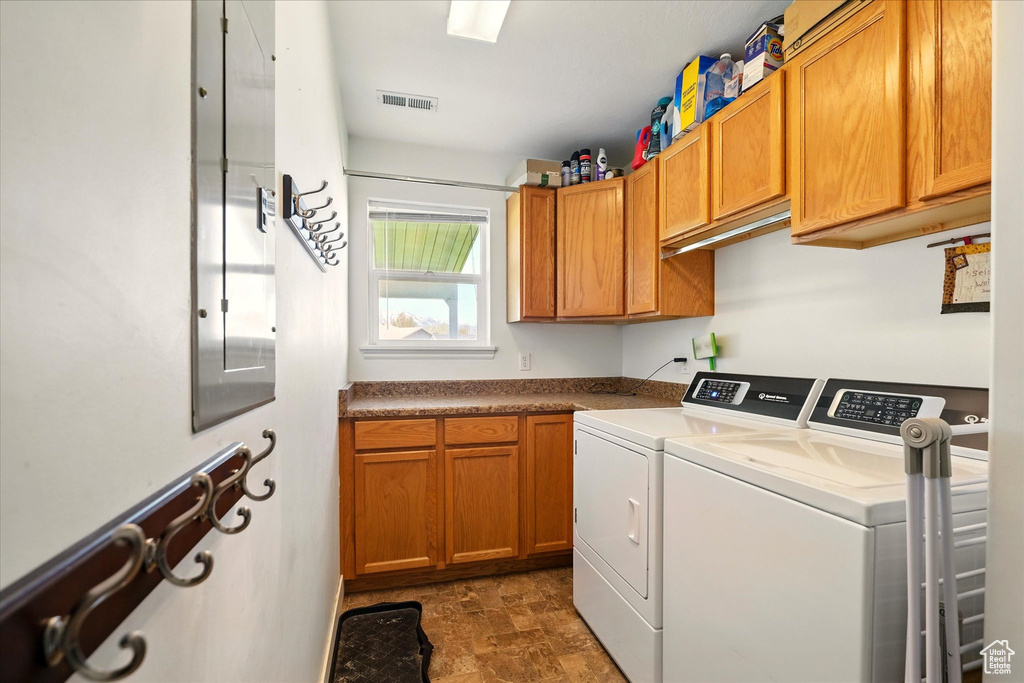 Clothes washing area with visible vents, washer and clothes dryer, cabinet space, and stone finish floor