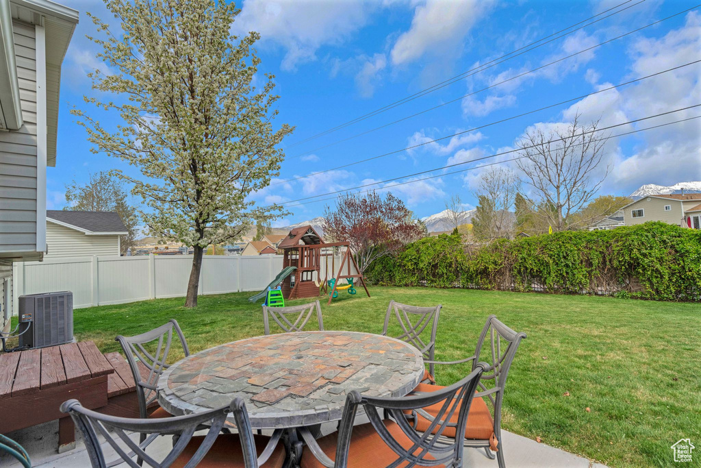 View of patio / terrace with central AC unit, a playground, a fenced backyard, and outdoor dining space