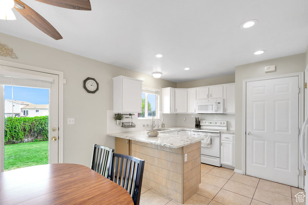 Kitchen featuring white cabinets, a sink, white appliances, a peninsula, and decorative backsplash