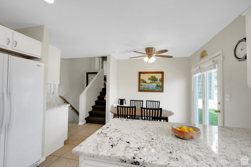 Kitchen with freestanding refrigerator, light tile patterned flooring, light stone countertops, ceiling fan, and white cabinets