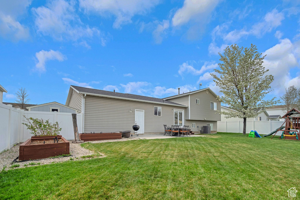 Back of house with a garden, a lawn, a patio area, a fenced backyard, and a playground