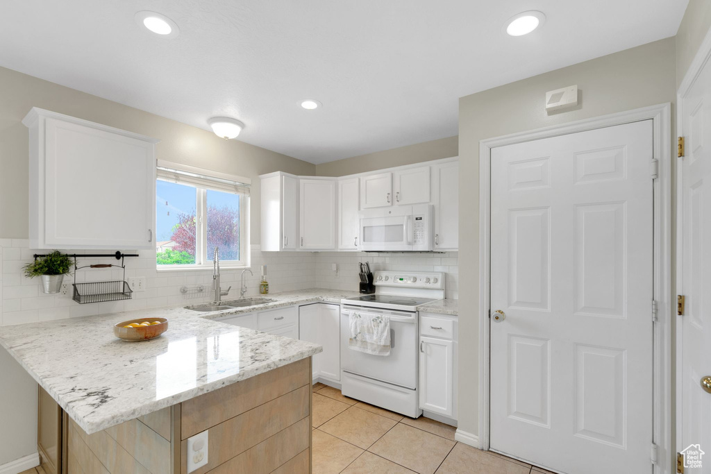 Kitchen featuring decorative backsplash, a peninsula, white appliances, light stone counters, and a sink