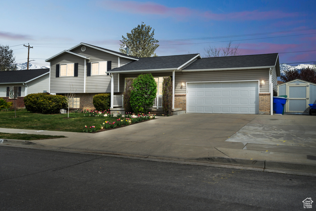 Split level home featuring a garage, a front yard, brick siding, a storage shed, and driveway