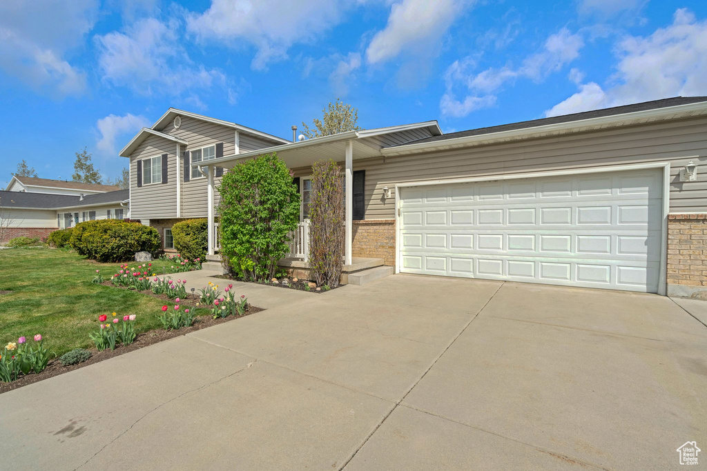 Split level home featuring brick siding, a garage, a front yard, and concrete driveway