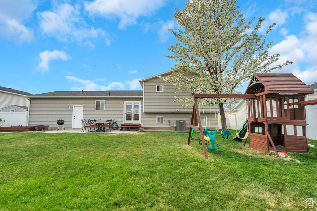 Back of property with fence, a patio area, a playground, a lawn, and central air condition unit