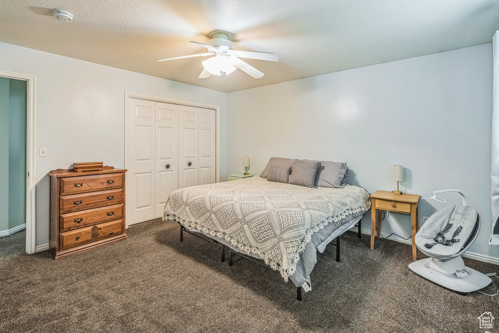 Bedroom with baseboards, a ceiling fan, a closet, and dark colored carpet