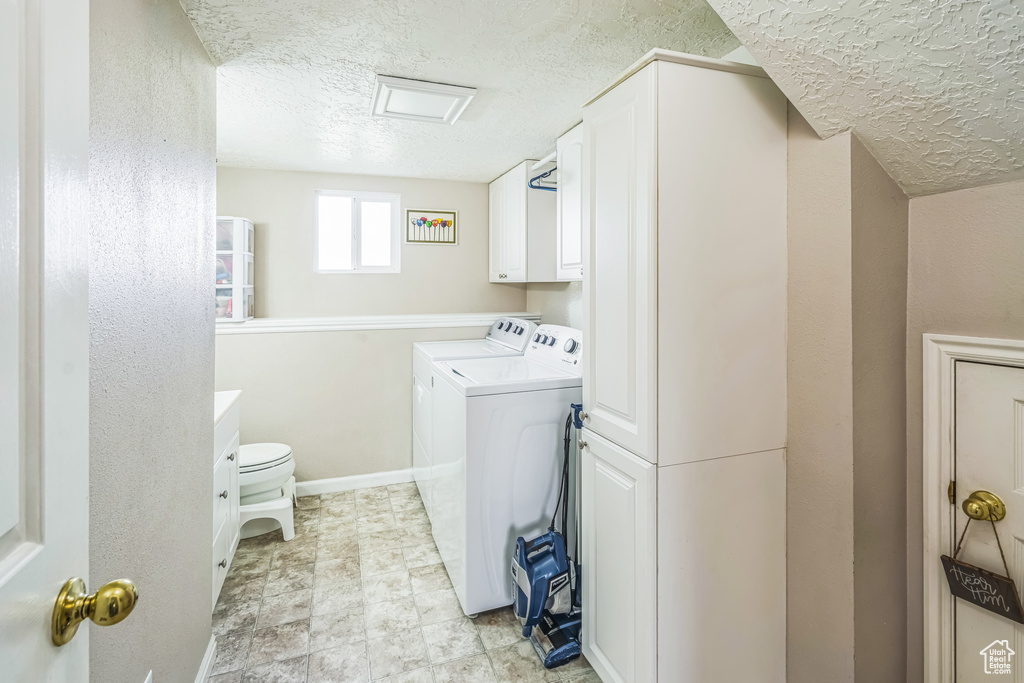 Laundry room featuring cabinet space, a textured ceiling, washing machine and dryer, and baseboards